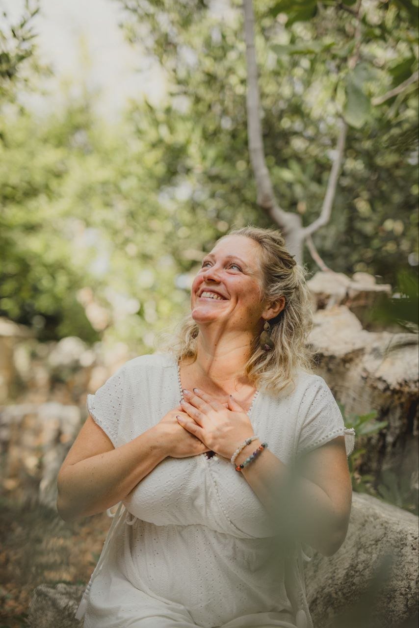 Sarah lächelt im Grünen, die Hände auf ihrem Herzen.
